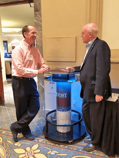 Business men leaning on cell phone charging table with branding at a trade show meeting