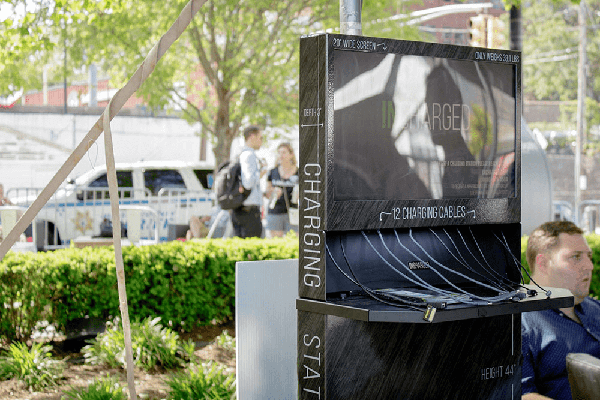 cell phone charging station with digital signage in front of greenery at event