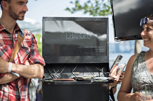 Man and woman smiling standing next to phone charging kiosk outside