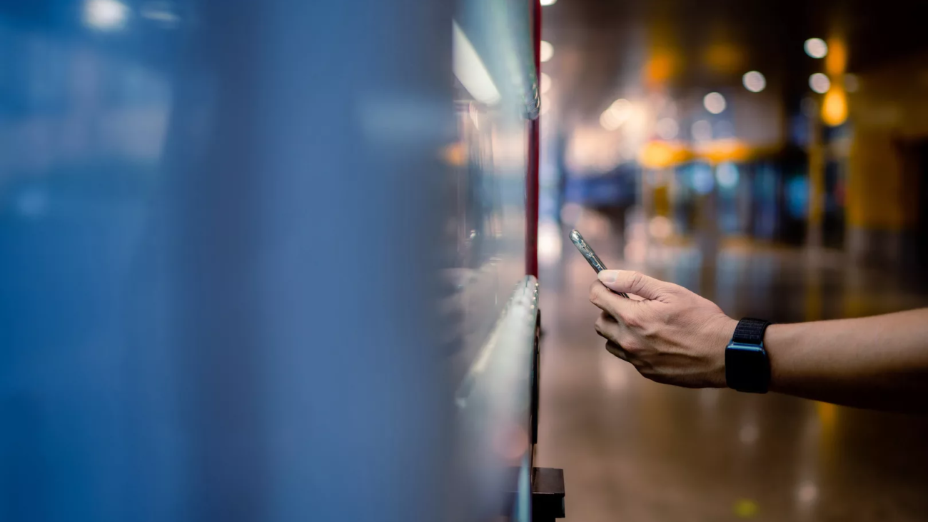 Asian man paying with smartphone to vending machine.