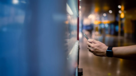 Asian man paying with smartphone to vending machine.